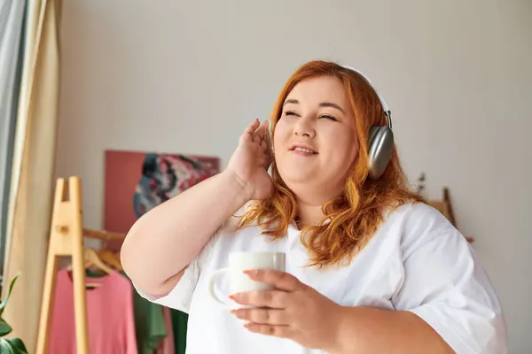 Красивая женщина plus size наслаждается любимыми мелодиями, потягивая кофе дома. — стоковое фото