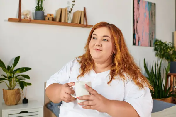 A plus size woman with wavy hair savors her tea while surrounded by plants and a warm atmosphere. — Stock Photo