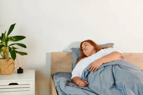 Una hermosa mujer de talla grande descansa tranquilamente en su cama, envuelta en suaves mantas, exudando tranquilidad. - foto de stock