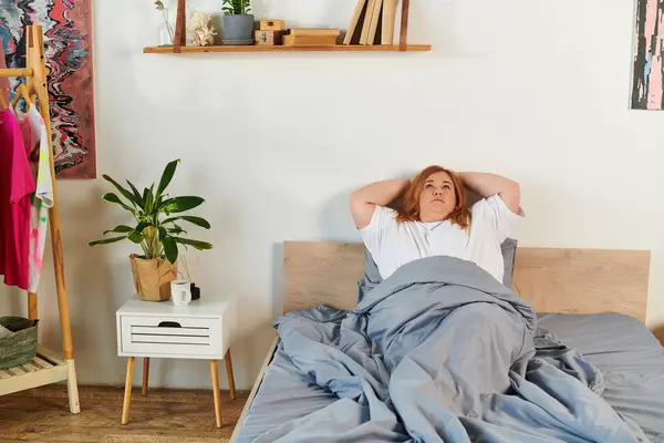 Женщина plus size отдыхает в постели, наслаждаясь мирным утром в окружении уютного декора. — стоковое фото