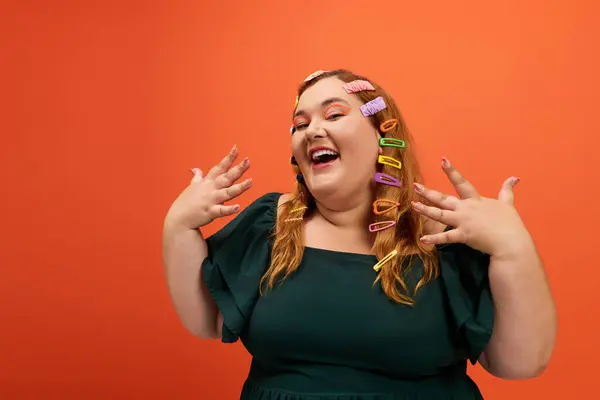 A smiling plus size woman with vibrant hair clips poses against a bright orange wall. — Stock Photo