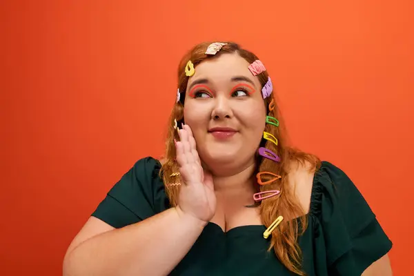 A cheerful plus size woman showcases her playful style with colorful hair clips against orange. — Stock Photo