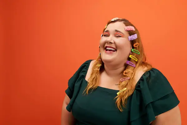 A joyful woman with colorful hair clips beams with happiness against a bold orange background. — Stock Photo
