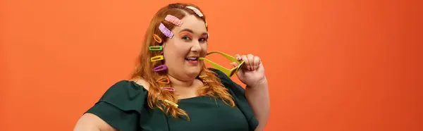 A joyful plus size woman poses playfully with hair rollers, radiating confidence. — Stock Photo