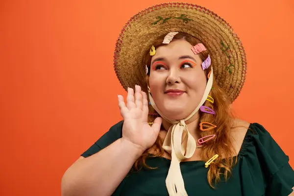 A cheerful plus size woman waves while wearing a large straw hat adorned with colorful clips. — Stock Photo