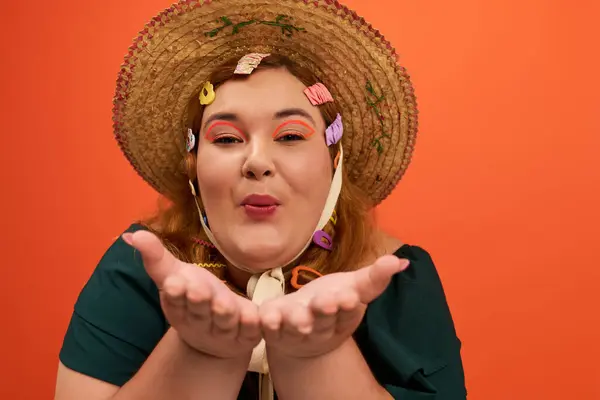 Une femme gaie plus la taille souffle baisers, exhibant ses accessoires colorés et la joie. — Photo de stock