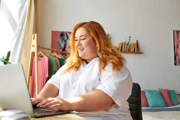 Женщина plus size наслаждается тем, что сидит на ноутбуке в окружении веселой обстановки. — стоковое фото