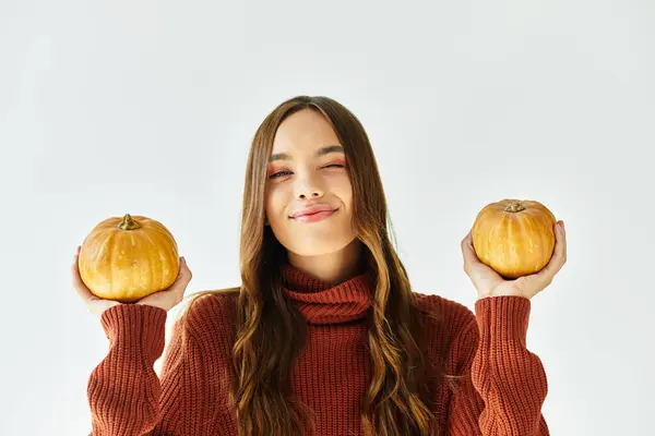 A young woman with long hair smiles cheerfully, showcasing pumpkins for Halloween festivities. — Stock Photo