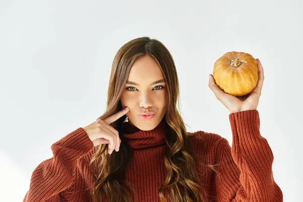 A stylish young woman playfully poses with a pumpkin, showcasing her Halloween spirit and charm. — Stock Photo