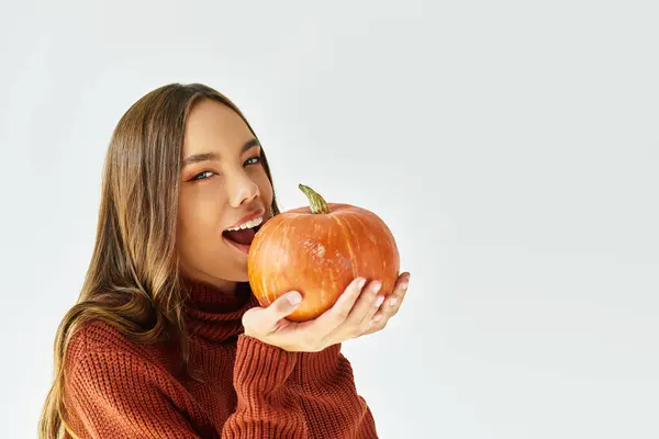 Eine junge schöne Frau, die für Halloween gekleidet ist, hält freudig einen großen Kürbis vor ihr Gesicht. — Stockfoto