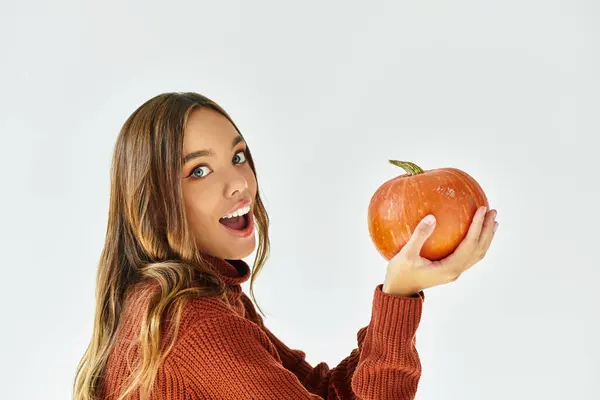 Joyful young woman in a Halloween outfit holds a bright pumpkin, celebrating the season. — Stock Photo
