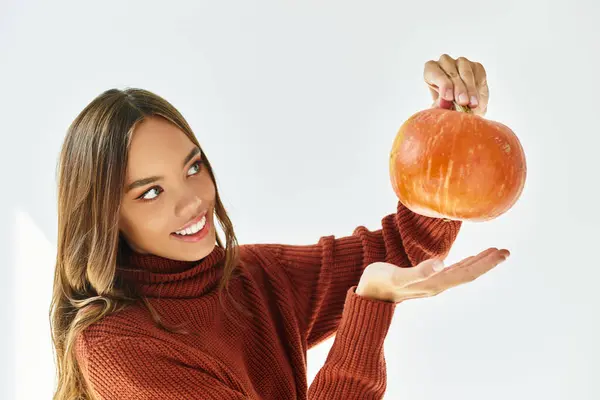 A cheerful woman joyfully holds a small pumpkin, embracing the festive spirit of Halloween. — Stock Photo