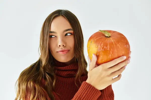 A beautiful young woman dressed in a Halloween outfit playfully holds a pumpkin indoors. — Stock Photo