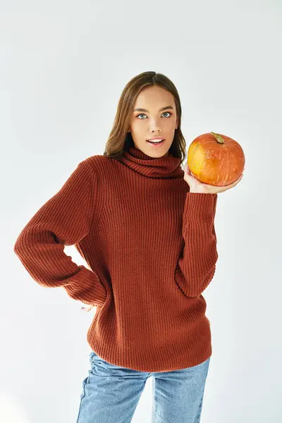 A young woman in a warm sweater showcases a pumpkin, embracing the Halloween spirit. — Stock Photo