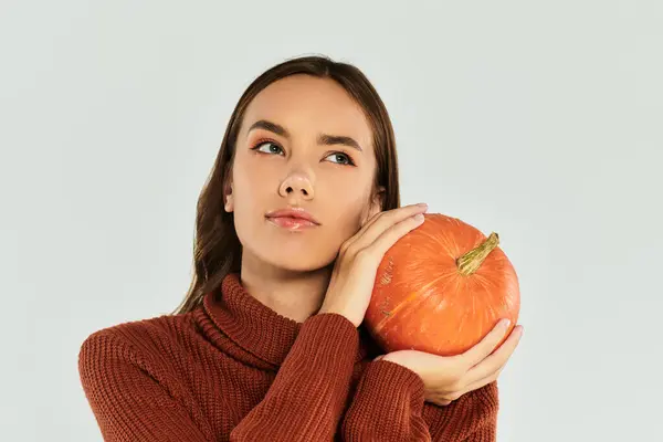 Una hermosa joven abraza una calabaza brillante mientras disfruta del espíritu de Halloween en el interior. - foto de stock