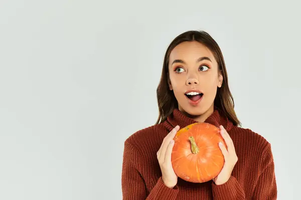 Eine überraschte junge Frau hält einen leuchtend orangefarbenen Kürbis in der Hand und umarmt den Halloween-Geist. — Stockfoto