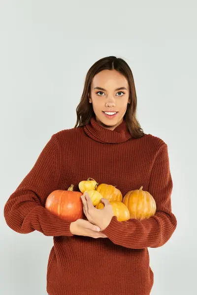 La jeune femme dans un pull chaud embrasse une collection de citrouilles vibrantes, célébrant l'automne. — Photo de stock