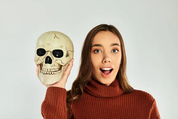 The beautiful young woman playfully holds a skull, showcasing her festive Halloween spirit. — Stock Photo