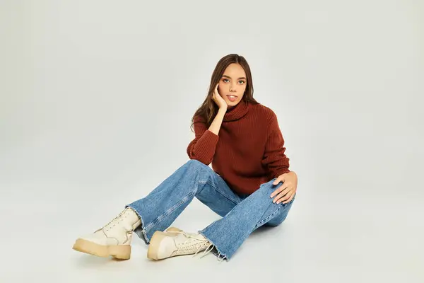 Young woman sits on the floor, dressed in a stylish sweater and jeans, radiating warmth. — Stock Photo