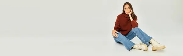 Appealing woman sits on the floor, dressed in a stylish sweater and jeans, radiating warmth. — Stock Photo