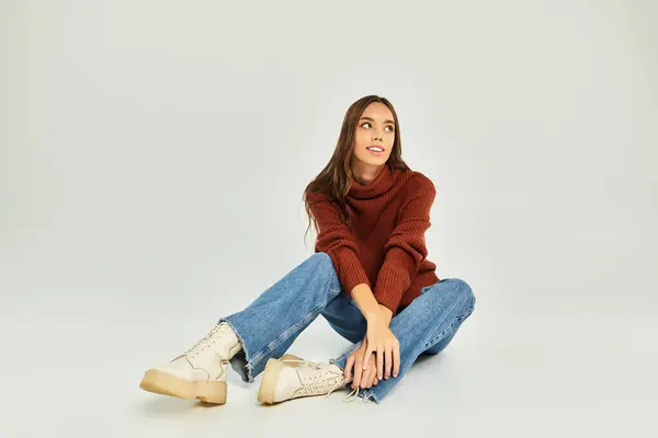 Attractive woman sits on the floor, dressed in a stylish sweater and jeans, radiating warmth. — Stock Photo
