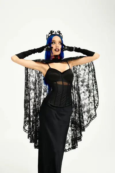 A young woman showcases her elaborate gothic costume with a flowing black cape and crown. — Stock Photo
