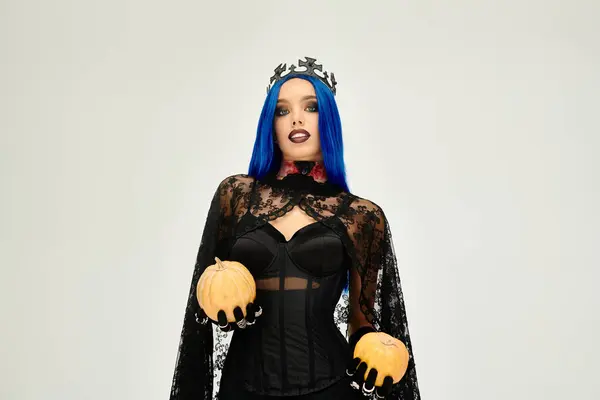A beautiful young woman dressed in a captivating Halloween outfit holds pumpkins, exuding charm. — Stock Photo