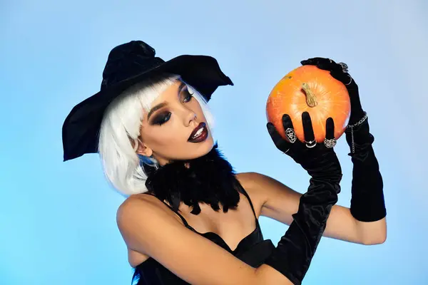 A graceful witch admires a pumpkin, capturing the playful spirit of Halloween. — Stock Photo
