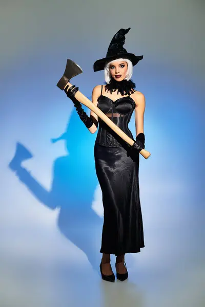 Dressed in an elegant witch costume, a young woman holds an axe striking a playful pose. — Stock Photo
