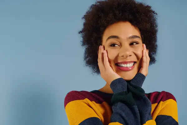In a vibrant sweater, a young woman beams with happiness, placing her hands on her cheeks. — Stock Photo