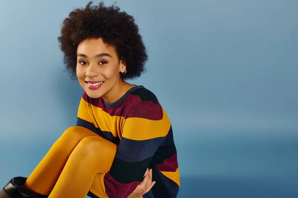 The young woman beams with joy, playfully posed in her colorful striped sweater. — Stock Photo