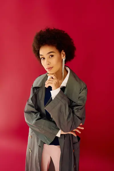 A young woman poses thoughtfully in a stylish outfit against a pink backdrop. — Stock Photo