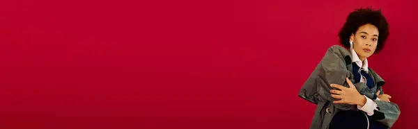 A young woman conveys strong emotions, wrapped in a stylish coat, with a striking red background. — Stock Photo