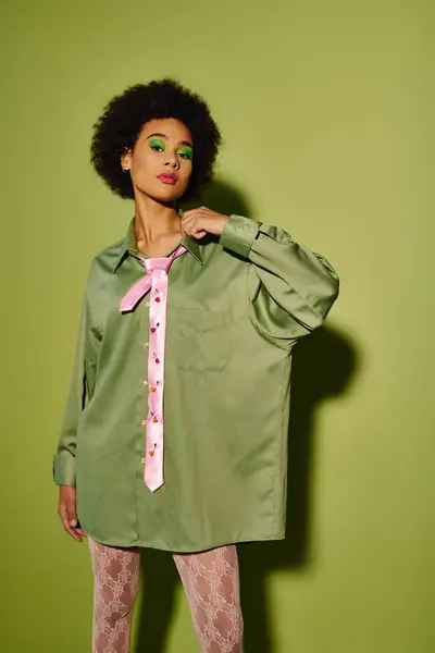 A young woman expresses emotions while posing in fashion forward attire against a vivid green wall. — Stock Photo
