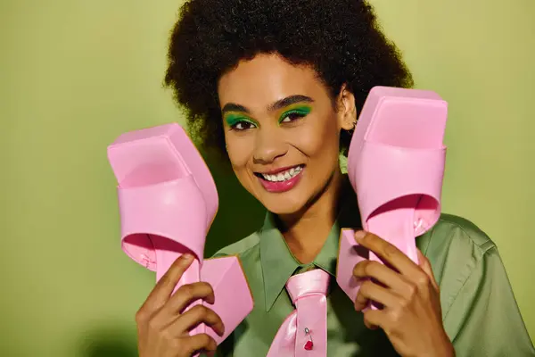 A joyful young woman holds pink heels, radiating confidence in a lively setting. — Stock Photo