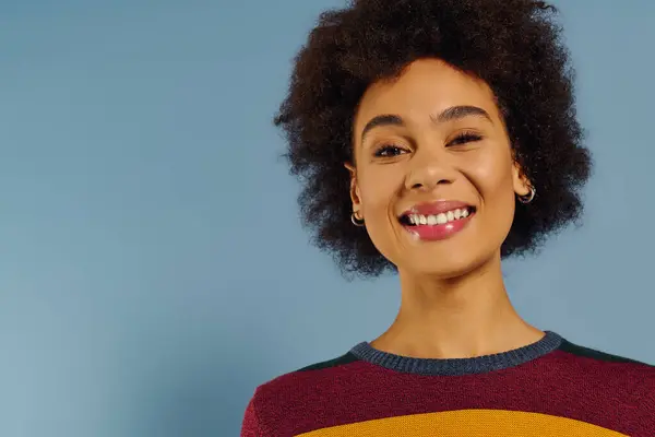 A young woman with curly hair smiles brightly, radiating happiness in a vibrant sweater. — Stock Photo