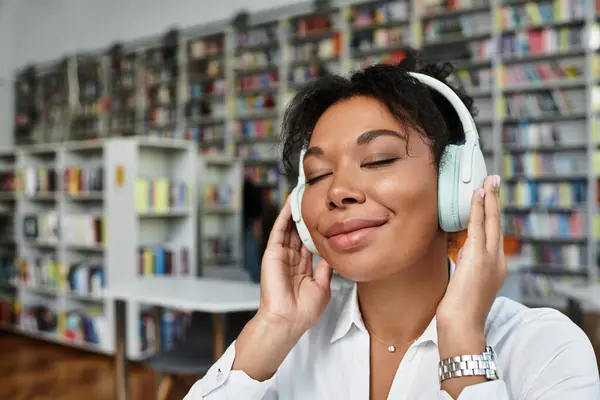 A joyful teacher experiences a moment of tranquility while using headphones in a library. — Stock Photo