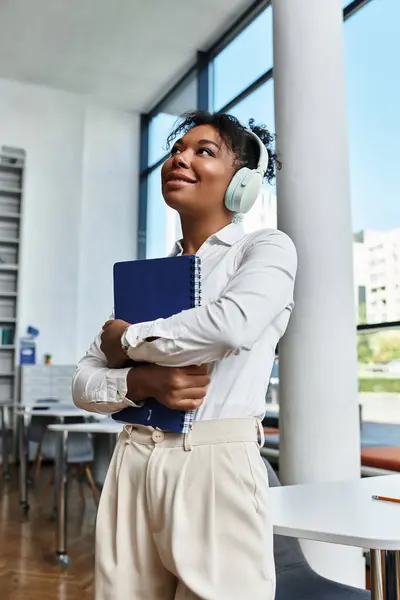 The African American teacher smiles as she holds her notebook, immersed in her creative thoughts. — Stock Photo