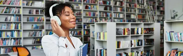 A devoted teacher listens to music while focused at a vibrant library full of books. — Stock Photo