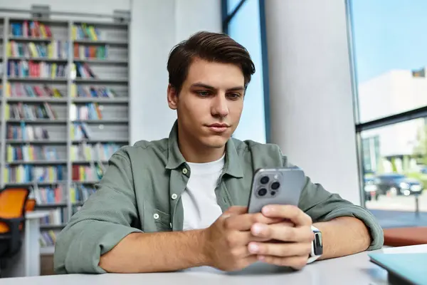 A focused student studies intently while using his smartphone in a vibrant library setting. — Stock Photo