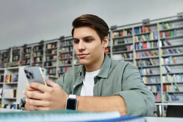 Uno studente concentrato è impegnato con il suo smartphone mentre studia nella biblioteca universitaria. — Foto stock