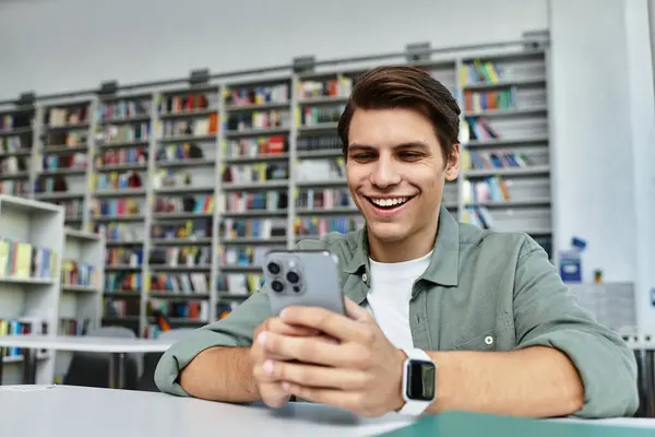 A focused student smiles while browsing learning material on his smartphone in the library. — Stock Photo