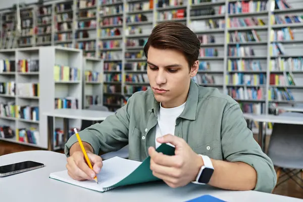 Intense young man diligently studying with notebooks in a tranquil university library environment. — Stock Photo