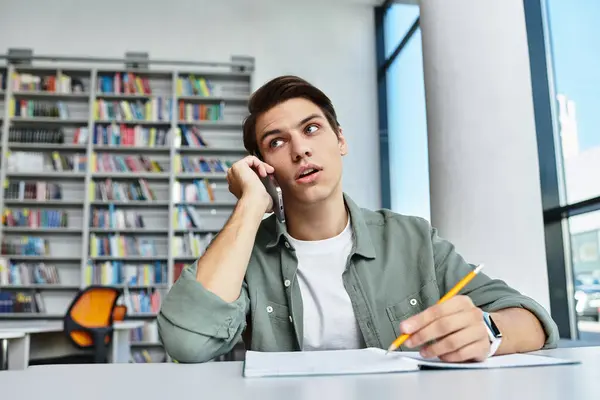 A dedicated student takes notes while on a call in a modern library filled with books. — Stock Photo