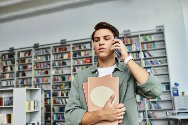A dedicated student is studying intently on the phone while holding documents in a library. — Stock Photo