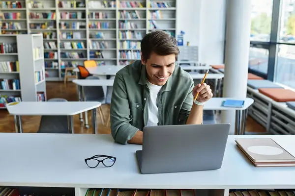 A focused student engages with his laptop, surrounded by books in a bright library. — Stock Photo