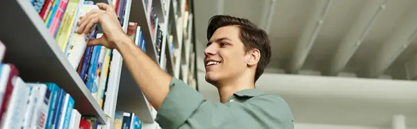 A focused young man eagerly explores shelves, selecting books to support his learning journey. — Stock Photo