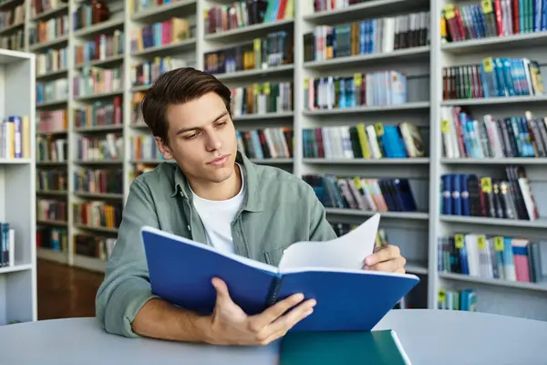 Красивый студент сосредоточен на учебе, окруженный полками с книгами.. — стоковое фото