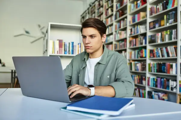 A diligent student concentrates on his studies at a library desk filled with books and notes. — Foto stock