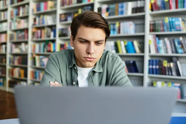 Ein fokussierter junger Mann studiert in einer Bibliothek, umgeben von unzähligen Büchern. — Stockfoto